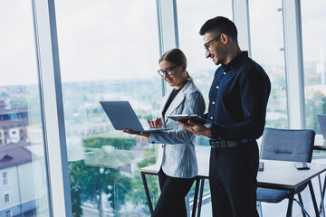 Beautiful businesswoman standing with Caucasian male colleague watching laptop screen and talking with businessman in office. Business relations between colleagues