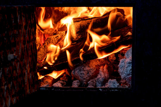 Burning firewood in fire-box of fireplace in country cottage. Metal fireplace for burning wood and heating a room in a rural area