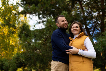 a happy husband joyfully hugs his wife against the backdrop of an autumn forest
