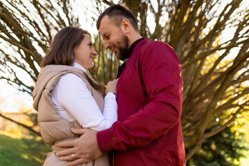 an adult married couple stand to each other against the background of a branchy autumn tree