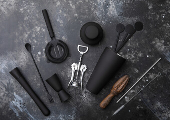 Black matt steel cocktail shaker,strainer,jigger and plastic stirrers with muddler on black stone background with manual wooden juicer.
