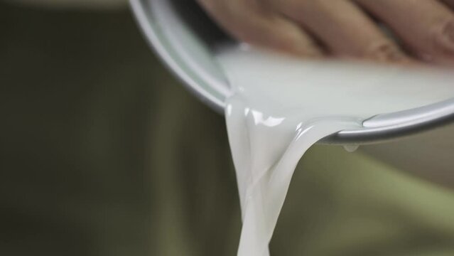 Washing raw white Thai jasmine long grain rice pouring out white cloudy starchy water liquid from the bowl in slow motion.