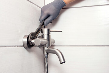 A plumber using a wrench installs a faucet in the bathroom