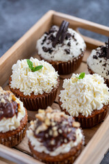 Cupcakes and muffins placed in wooden box. Chocolate and creme with nuts. Fresh home make baked sweets.