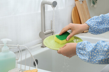 Woman washing plate above sink in kitchen, closeup