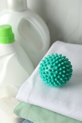 Fototapeta na wymiar Turquoise dryer ball on stacked clean towels near laundry detergents