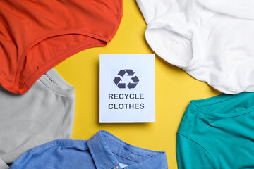 Different clothes with recycling label on yellow background, flat lay