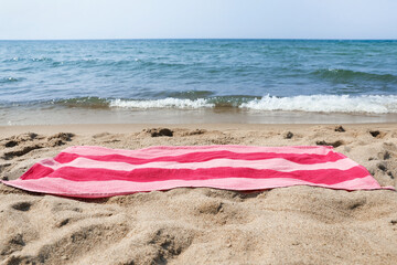 Fototapeta na wymiar Pink striped towel on beach sand near sea