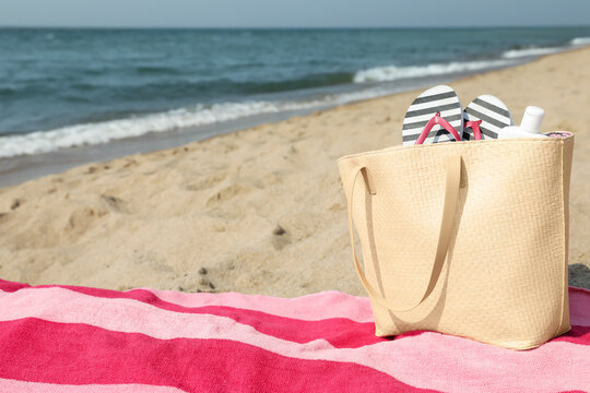 Pink striped towel with bag, flip flops and sunscreen on beach