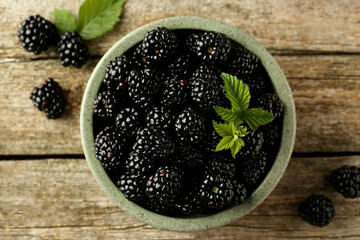 Bowl and fresh ripe blackberries on wooden table, flat lay