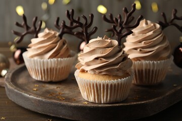 Tasty Christmas cupcakes with chocolate reindeer antlers on wooden tray, closeup