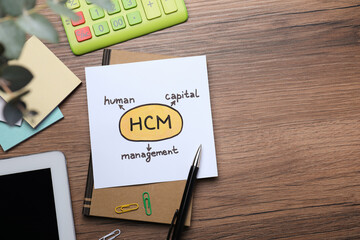 Paper with HCM abbreviation and space for text on wooden office table, flat lay. Human Capital...