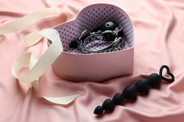 Heart shaped gift box with different sex toys and ribbon on pink silk fabric