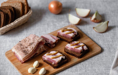 rustic natural food, on a linen tablecloth a wooden board, on it are ready-made sandwiches from black rye bread and lard with mustard and boiled eggs.