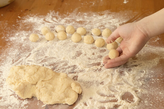child's hand lays out a lot of small dough balls next to a large piece of dough on a wooden table showered with flour