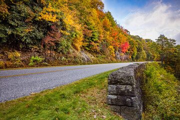 Gray stone wall lines the blue ridge parkway with fall color on the other side of the road