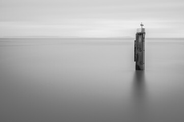 Moody, black and white long exposure, of a single, old wooden post, in the ocean. Room for copy.