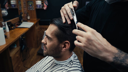 Barber cutting hair of customer in hairdressing cape in barbershop.