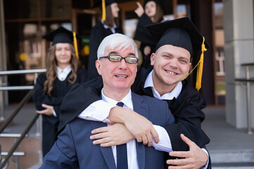 Fototapeta premium Father and son embrace at graduation. Parent congratulates university graduate.
