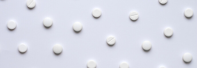 Medical background of many tablets or pills on a white background. Medical pharmacy and medicine concept with copy space. Horizontal banner on a medical theme. A scattering of white pills.