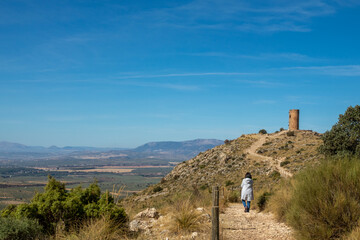 Woman walking along the path that goes up to the old Arab tower of Deifontes (Granada, Spain) on a sunny autumn morning