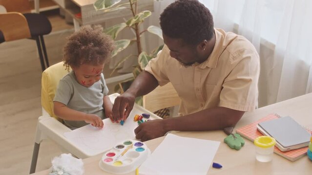 From above shot of Black man and his pretty toddler daughter drawing together with wax crayons at home