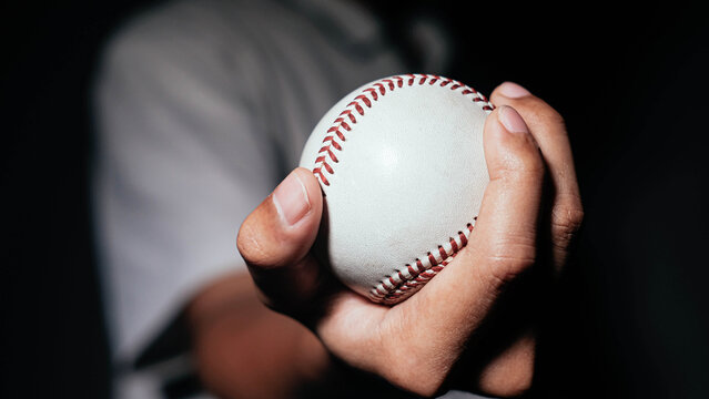 Selective focus of man holding baseball ball isolated on black background.