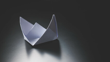 Several paper boats are on the table. one of them is red concept of leadership.
