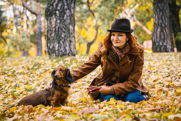 Young red-haired woman posing in the park with a red dachshund dog. 