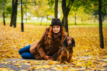 Young red-haired woman posing in the park with a red dachshund dog. 