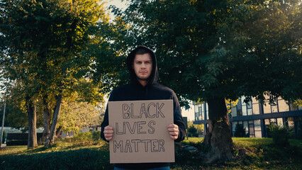 young man in hoodie holding placard with black lives matter lettering outside.