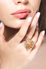Fashion, style, jewelry and make-up concept. Close-up studio portrait of beautiful and sexy woman face with fancy golden ring. Model holding hand with ring near her lips