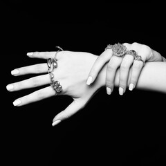 Fashion, make-up and jewelry concept. Studio portrait of beautiful woman hands with beautiful manicure and many various fancy rings on her fingers in black studio background. Black and white image
