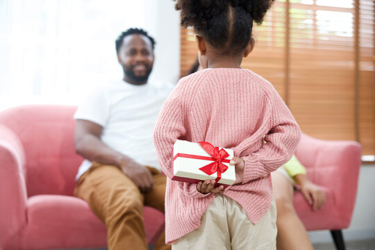 Back Girl Hiding Present Or Gift Box Giving To Mom And Dad Sitting On Sofa