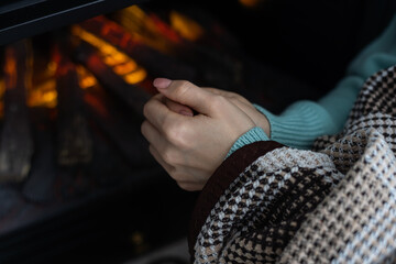 Woman rubbing hands and heating in front a fire place at home in winter.