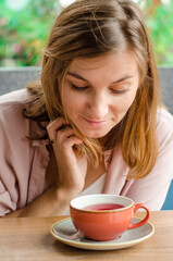 Cheerful interested woman with blond hair looking into a cup of red tea, what is in it