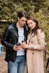 young woman and man in stylish outfits standing with closed eyes and holding coffee to go.