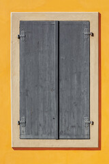 Rectangular window is covered with gray wooden shutters against a yellow wall. From the Window of the World series.