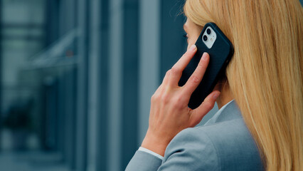 Back view close-up blonde caucasian businesswoman talking on mobile phone answering business call remotely communicates with client using smartphone woman leader standing outdoors speaks on telephone