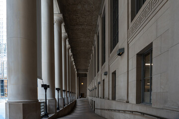 Diminishing perspective of exterior dark hallway with columns on one side and wall with windows on...