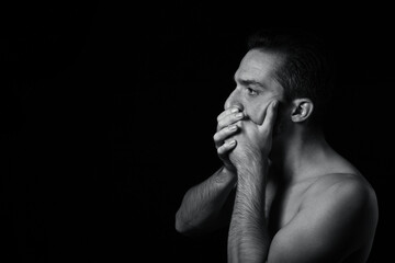 The man covers his mouth with his hands. Black-white portrait of a man on a black background.