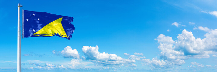 Tokelau flag waving on a blue sky in beautiful clouds - Horizontal banner