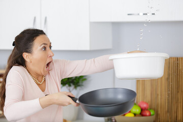 worried woman holding bucket while water droplets leaking from ceiling