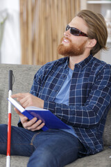 blind man reading book written in braille on sofa