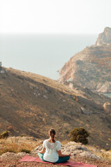 Naklejka premium An elderly woman practices yoga on a mountain overlooking the sea
