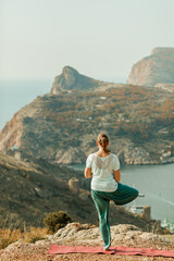 Fototapeta na wymiar An elderly woman practices yoga on a mountain overlooking the sea