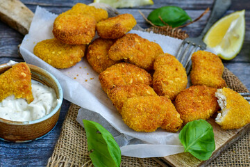 
 Crispy oven baked  chicken Nuggets  with garlic sauce.Breaded chicken fillets  with chilly peppers and fresh basil on wooden rustic background