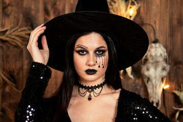 young girl in the image of a witch, wearing a black hat and a black dress with a make-up