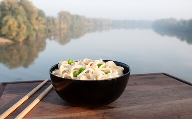 Vegetable noodles and chopsticks on a wooden board next to the river.