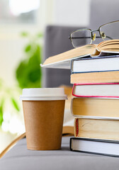A disposable paper coffee cup next to a stack of books. Vertical Format